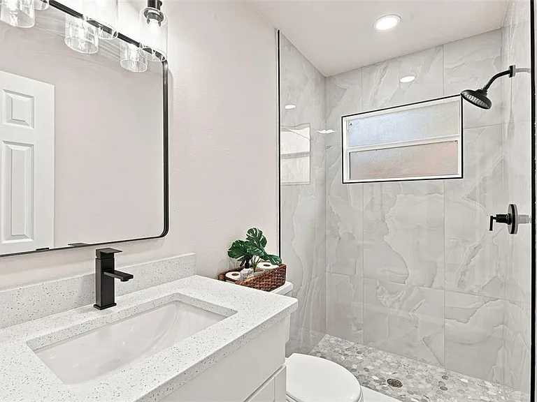 Renovated bathroom with quartz vanity, matte black fixtures, and marble-look tiled walk-in shower