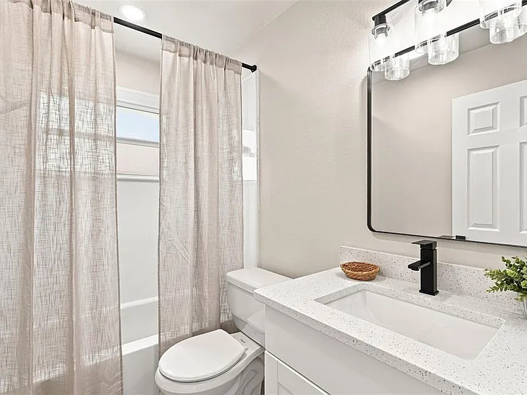 Renovated second bathroom with white vanity, black fixtures, and updated tub-shower combo